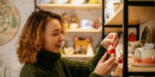 Woman in a green knit sweater choosing a handmade ceramic Christmas decoration in a festive shop, representing a small business insured for the season