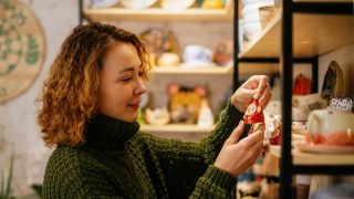 Woman in a green knit sweater choosing a handmade ceramic Christmas decoration in a festive shop, representing a small business insured for the season