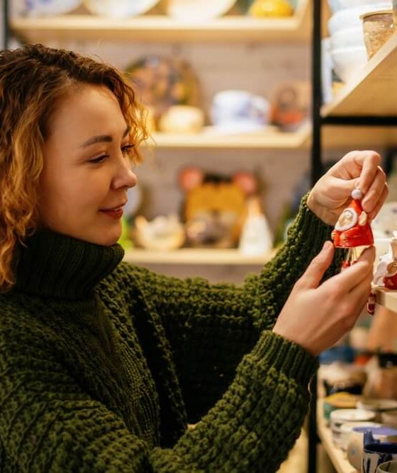 Woman in a green knit sweater choosing a handmade ceramic Christmas decoration in a festive shop, representing a small business insured for the season