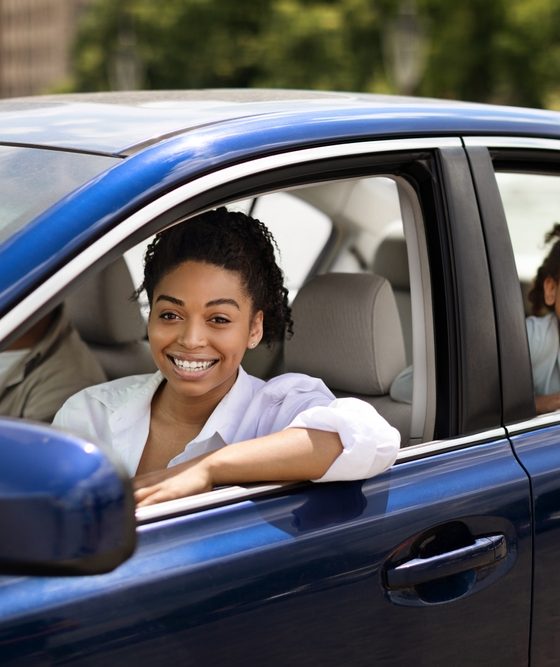 African American Family Posing Sitting In Blue Car In Urban Area. Mom And Daughter Driving New Auto Enjoying Ride Smiling To Camera, avoiding auto insurance mistakes by purchasing coverage.