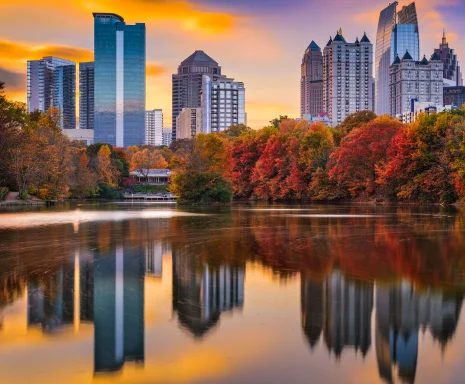 Skyline, cityscape, sunrise or sunset of downtown Atlanta, Georgia with ferris wheel: Cheap car insurance in The Peach State. Piedmont Park skyline in Dogwood City in autumn. View of a lake, downtown Atlanta, and reflection of trees and buildings in the water. Cheap car insurance in Georgia.