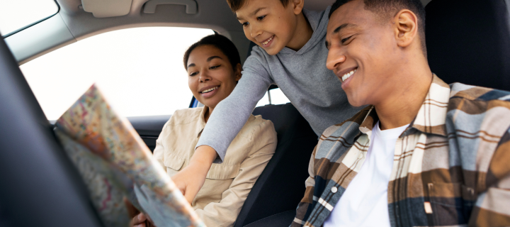 Happy family of three with boy looking at map sitting in car and choosing destination.