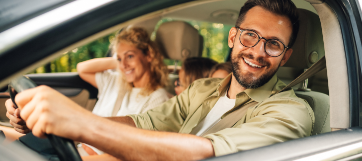 Portrait of a handsome smiling man driving a car. Father enjoying road trip on weekend and traveling by automobile with his family. Holiday and travel concept.