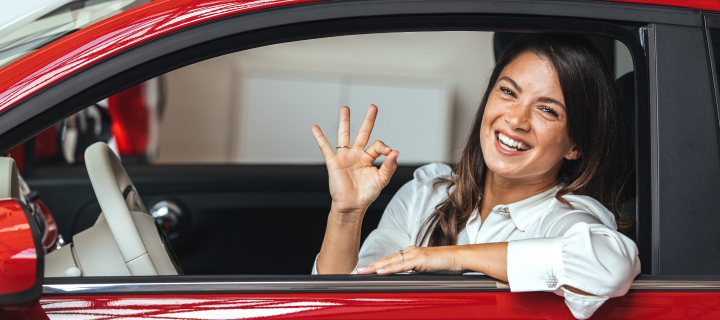 Happy woman driving a car with thumbs up. Beautiful girl looking through the car window and showing ok. Business woman through the car window showing ok.