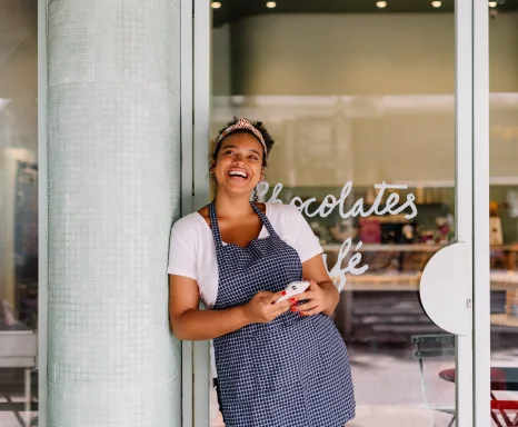 Successful cafe owner, a young woman, stands in her restaurant using a smartphone.