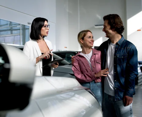 A female car dealer uses a digital tablet to assist clients in the showroom. She engages with buyers, showcasing options and highlighting personalized service during their car purchase journey.