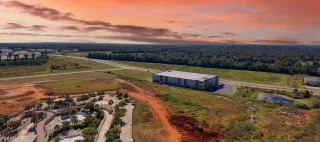 an aerial shot of the city of Warner Robins Georgia with vast miles of lush green trees, grass and plants with buildings and highways with cars driving and powerful clouds at sunset.