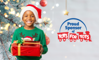 A cheerful child in a Santa hat and green sweater holds a red gift next to the Toys for Tots logo and the text “Proud Sponsor of Toys for Tots.”